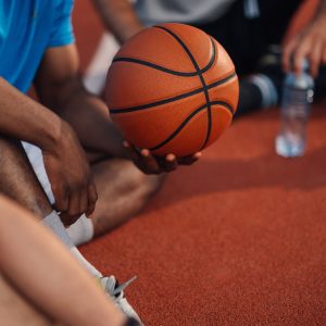 Image depicts an athlete sitting on the basketball court holding a ball, focusing on sport and teamwork