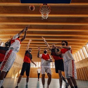 Low angle view of a group of professional diverse players training basketball together and standing under the hoop during practice and preparing for a match in a sports hall. Copy space.