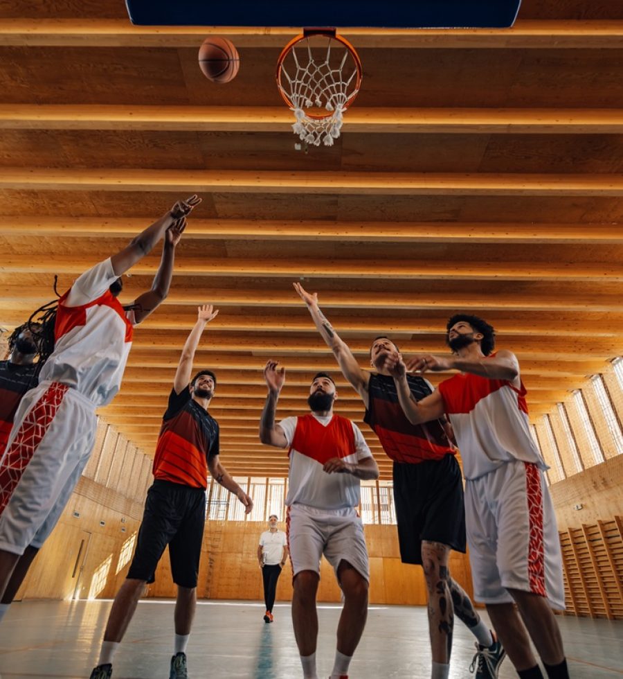 Low angle view of a group of professional diverse players training basketball together and standing under the hoop during practice and preparing for a match in a sports hall. Copy space.